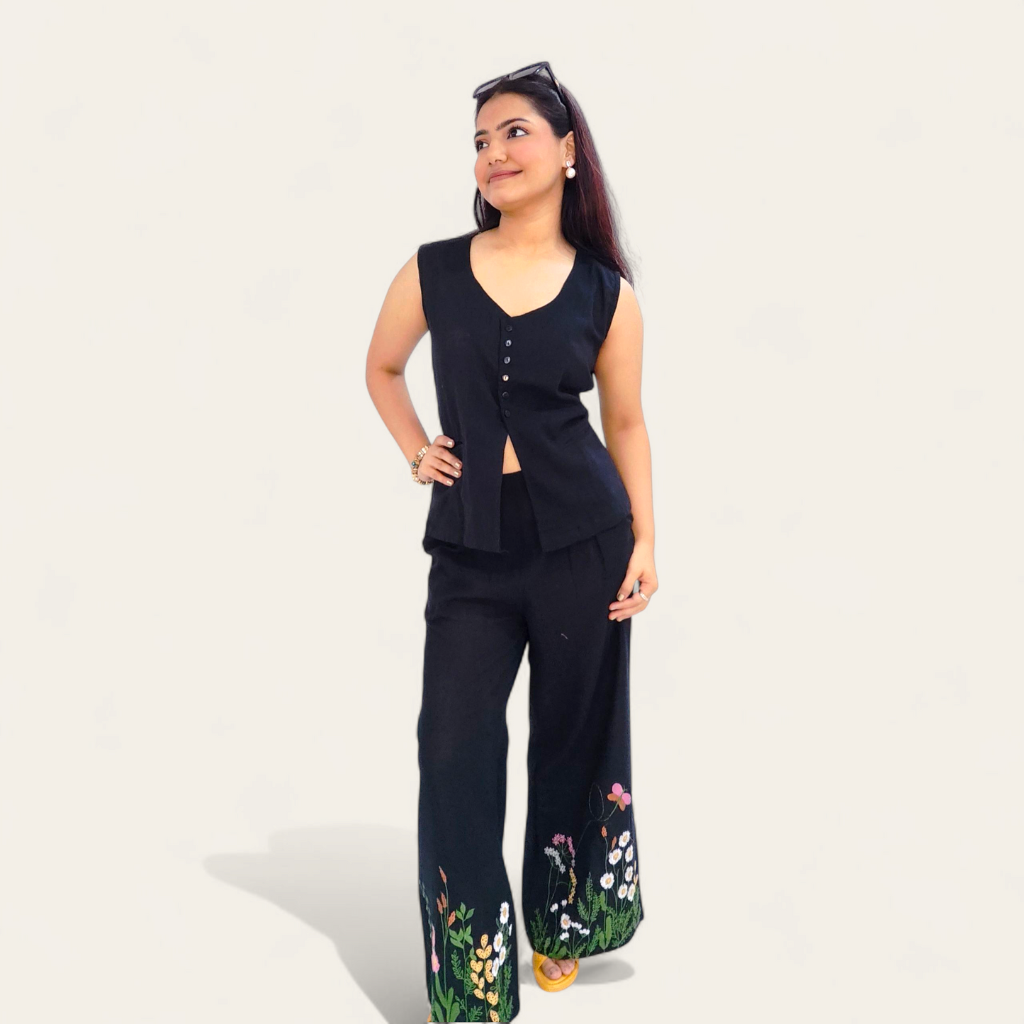 Woman wearing a black outfit with floral pants on a plain background