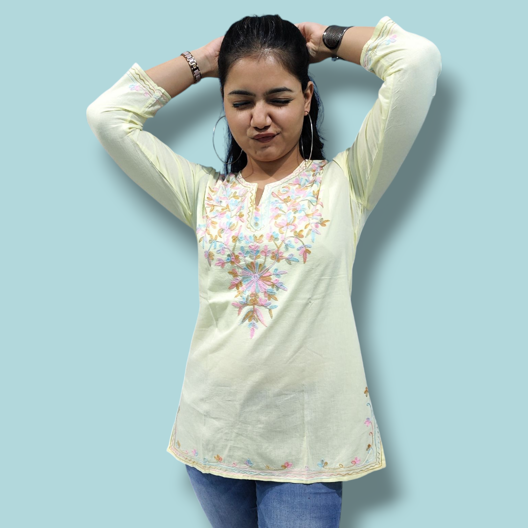 Woman wearing a light-colored embroidered top against a blue background