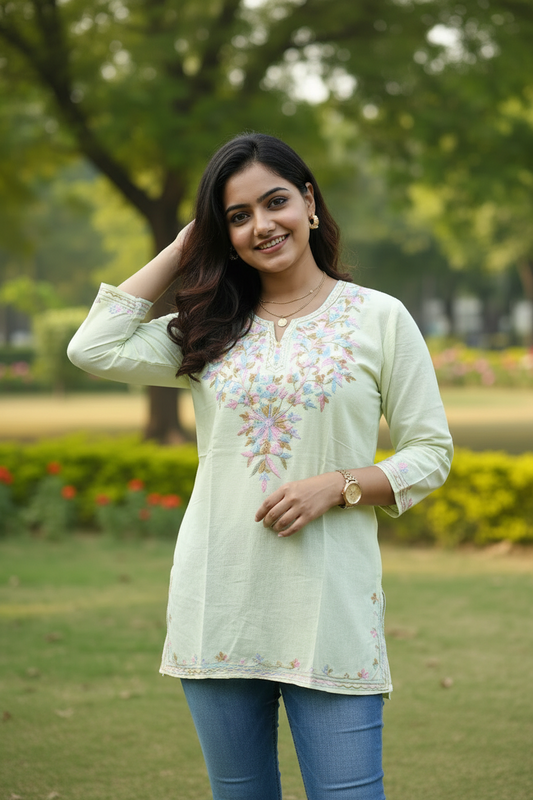 Woman wearing a light yellow embroidered top and blue jeans in a park setting